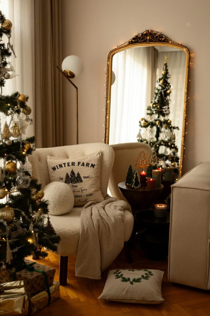 Butaca blanca con manta y cojín junto a un espejo dorado y un árbol de Navidad iluminado
