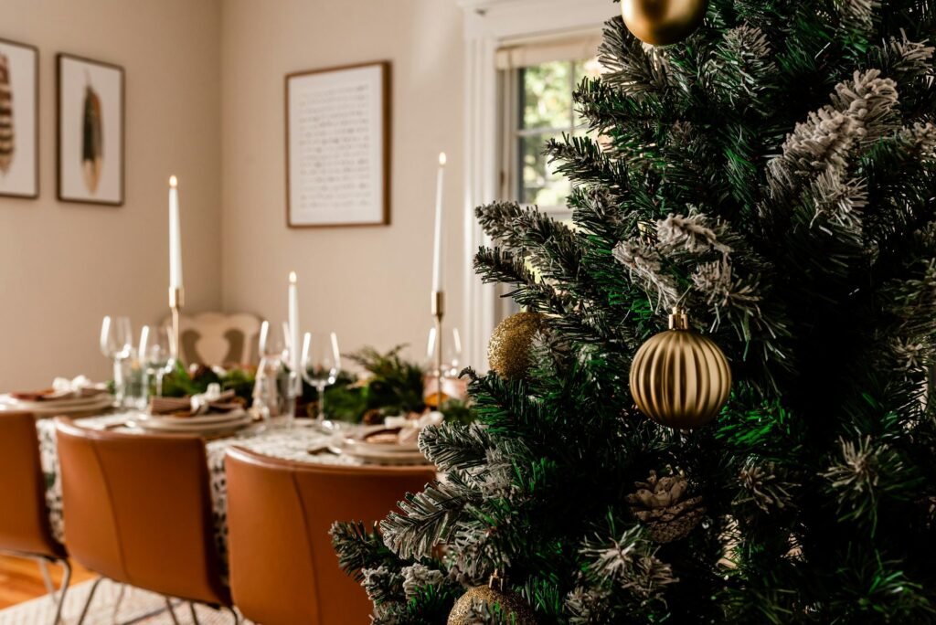Ramas nevadas de un árbol de Navidad en primer plano y, al fondo, una mesa puesta para la cena