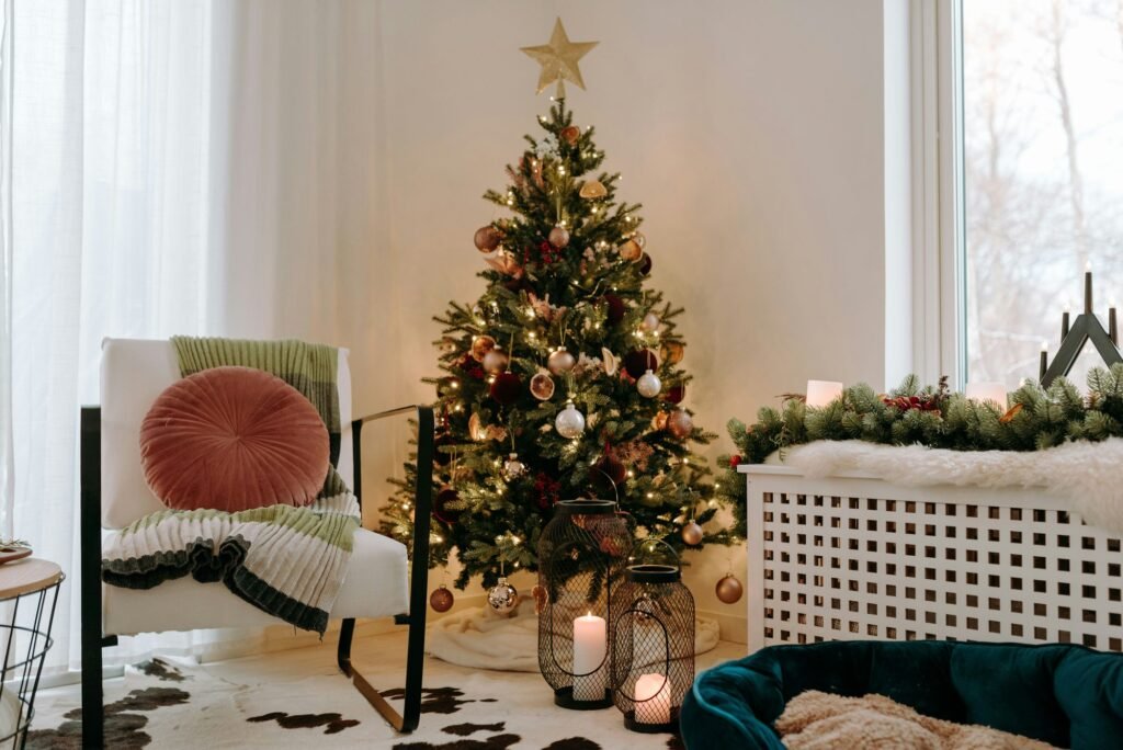 Árbol de Navidad con estrella dorada junto a una butaca con cojín rosa y una guirnalda sobre el radiador