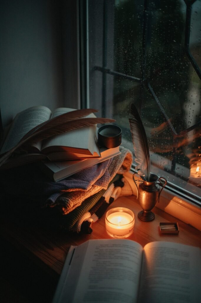 Libros abiertos y una vela encendida junto a una ventana con gotas de lluvia