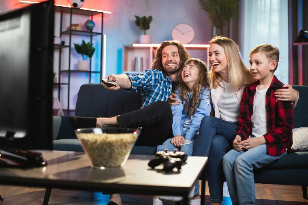 Familia riendo en el sofá frente al televisor con un cuenco de palomitas