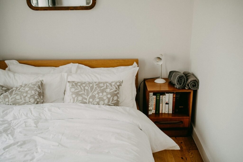 Dormitorio de invitados con ropa de cama blanca, cojines estampados y mesita de madera