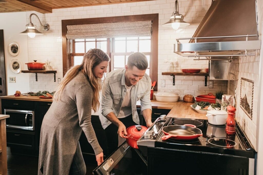 Pareja cocinando junta en una cocina con campana de acero y ollas rojas