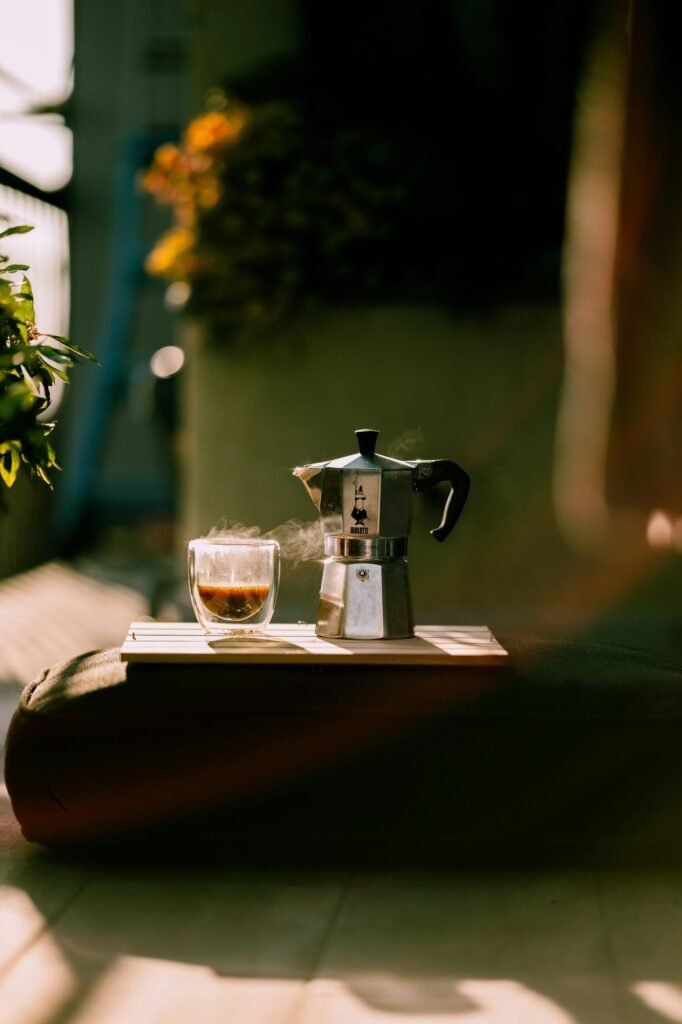 Cafetera italiana y taza de café sobre una pequeña mesa al sol