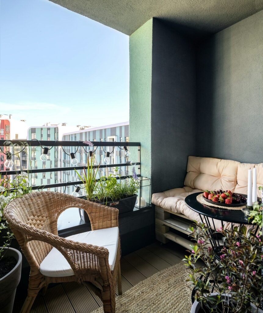 Balcón pequeño con sillón de mimbre, banco con cojines y plantas