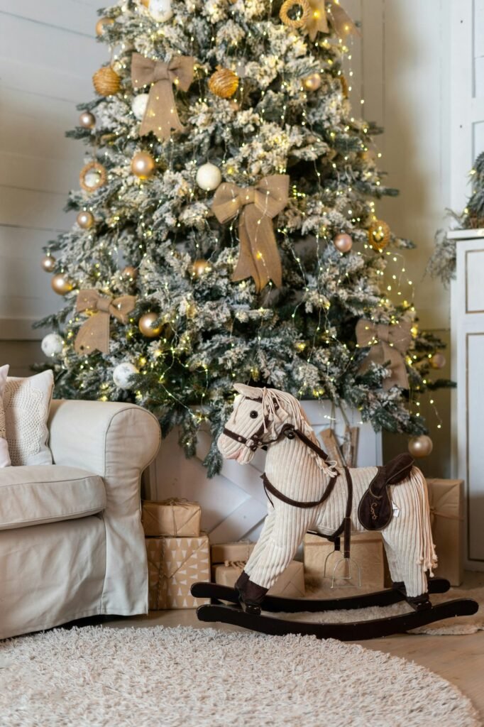 Árbol nevado con lazos dorados junto a un caballito balancín y un sofá blanco