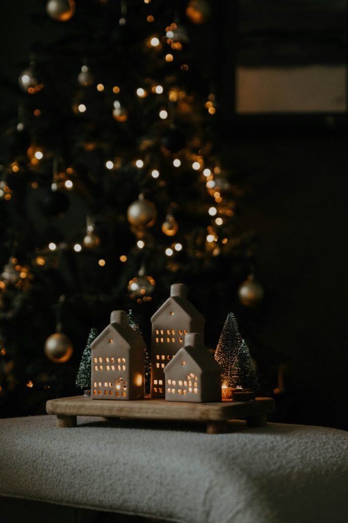 Casitas de cerámica iluminadas sobre una bandeja de madera delante de un árbol con luces