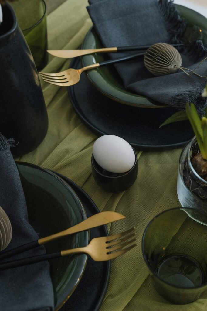 Mesa con mantel verde, platos oscuros y cubiertos dorados