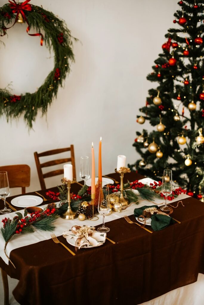 Mesa con mantel marrón, velas naranjas y candelabros dorados junto a un árbol de Navidad