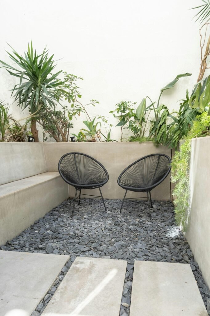 Pequeño patio con muros de hormigón, plantas y dos sillas de cuerda negras